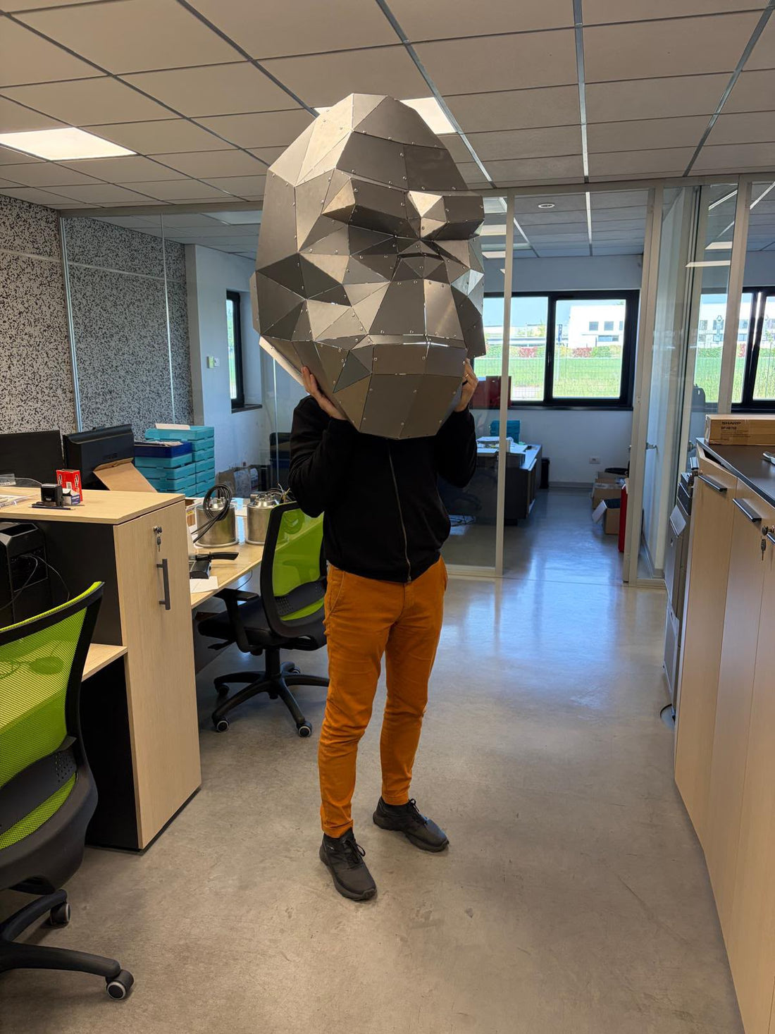 A person carrying the head of a six-metre low poly metal sculpture through an office, showing the scale of a large build
