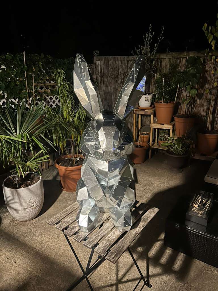 Riveted low poly metal rabbit sculpture on a garden table at night, finished in one weekend from a DXF template