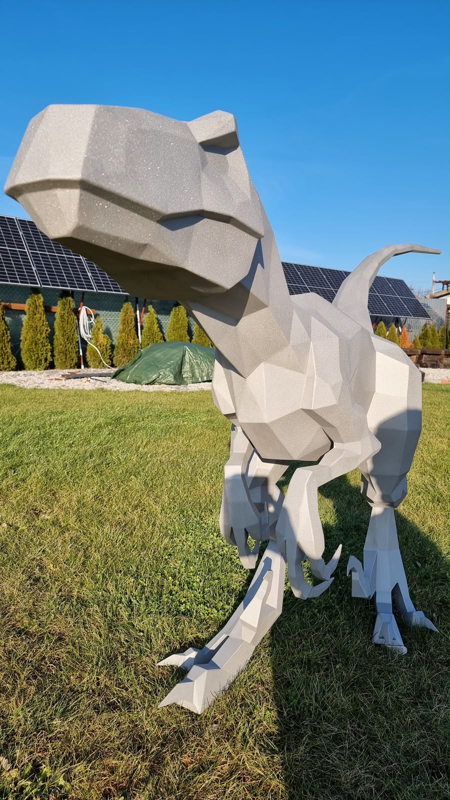 Large white low poly metal T-Rex sculpture standing on a lawn, cut and assembled at home from a DXF template